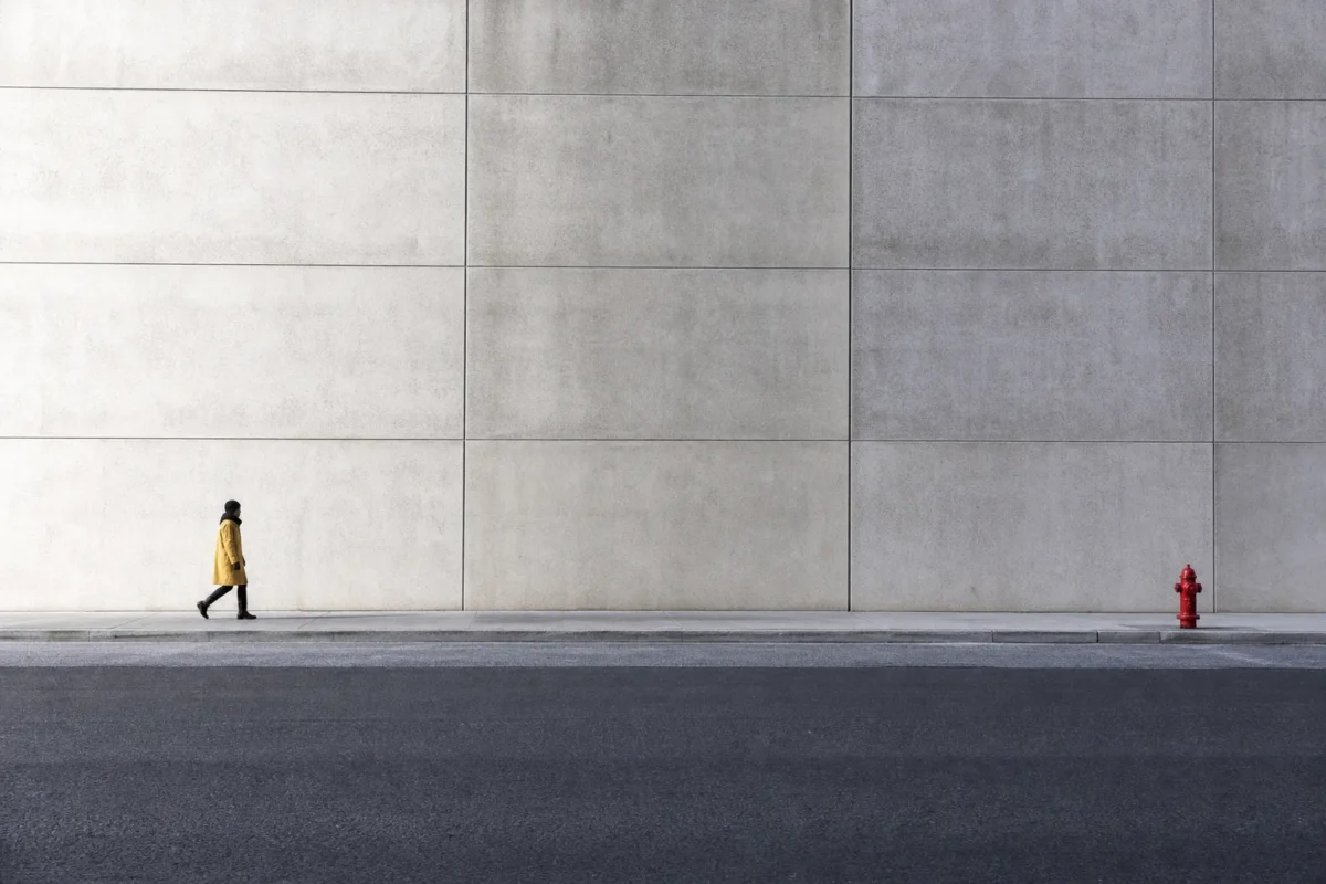 Small walking subject balanced by a large concrete wall and a red visual accent