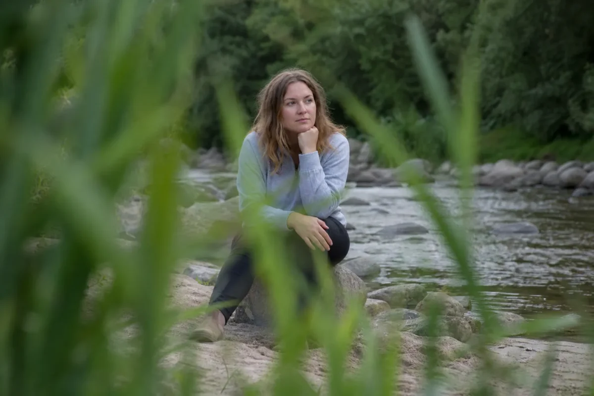 Portrait framed by soft foreground grass and leaves beside a river