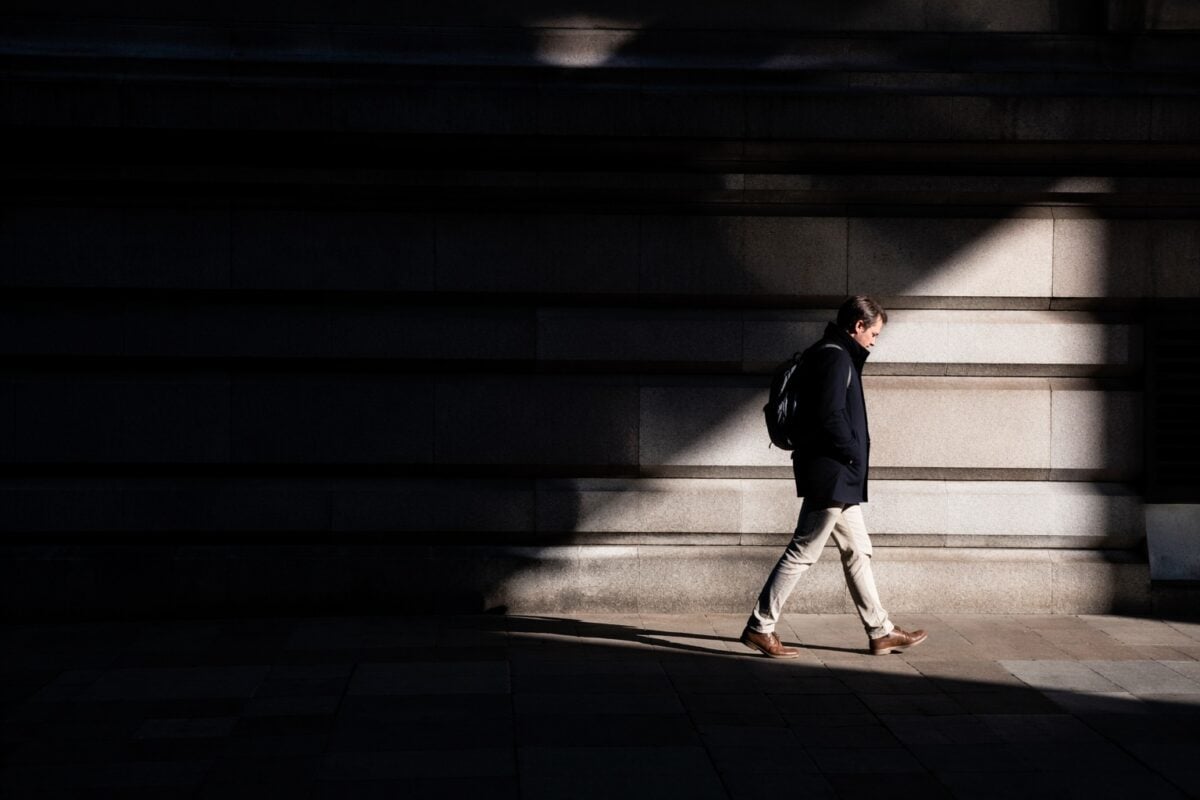 Person crossing a bright patch of light against deep shadow to create dynamic tension