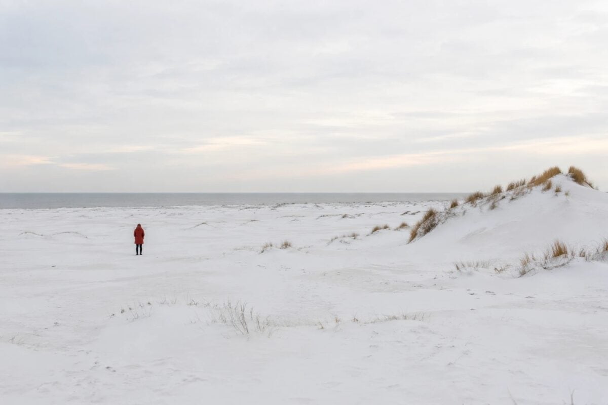 Person in a red coat holding visual weight inside a snowy negative space composition