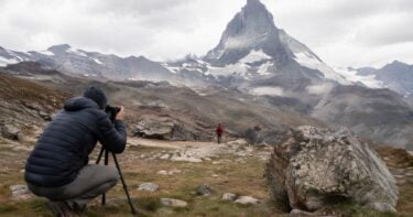 Photographer composing a landscape with foreground rock hiker and mountain peak forming a triangle