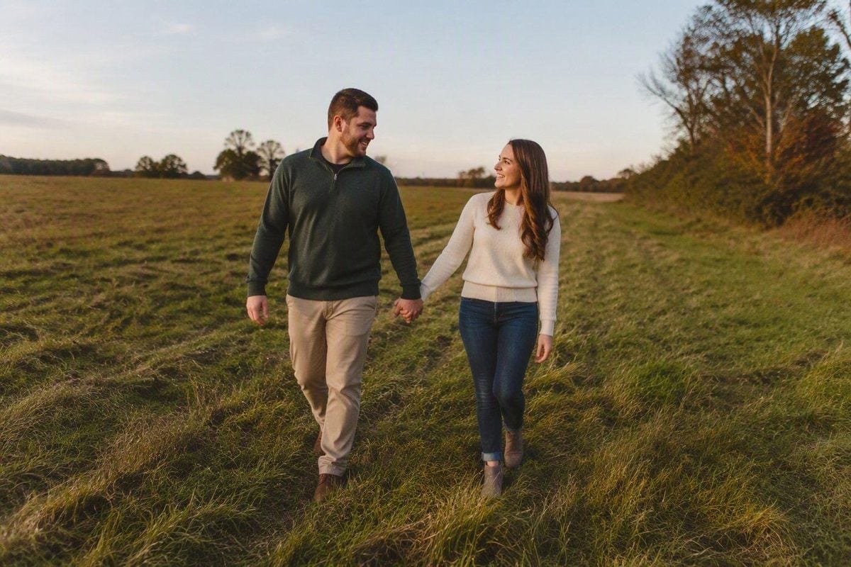 Engaged couple walking an open field in late-day light with space to move and reset